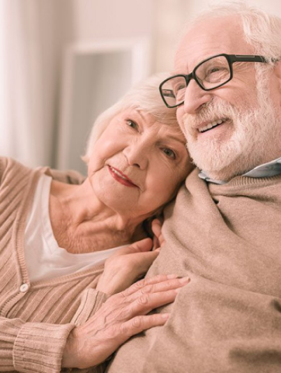 An older couple smiling while sitting on the couch in their serene and cozy living room.