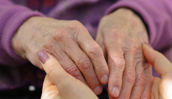 A woman's hands are touching a main older woman's hands.