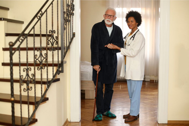 An elderly man and a nurse standing in front of a Nursing Home staircase.