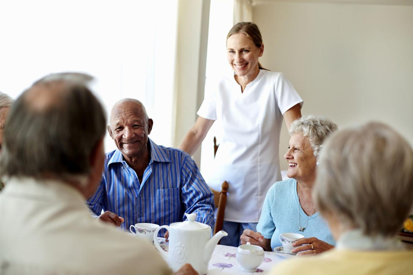 A group of elderly people sitting around a table with a nurse at an assisted living facility.